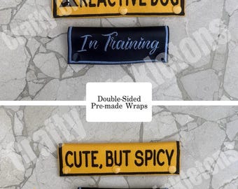May include: Four rectangular leash wraps with snap closures. Two are yellow with black text reading "REACTIVE DOG" and "CUTE, BUT SPICY". Two are black with light blue text reading "In Training". The wraps fit up to 1-inch wide leashes.