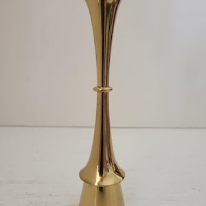 以下が含まれることがあります： 広がった上部と幅広のベースを持つ金色の金属製燭台。燭台は中央が狭い部分でデザインされています。