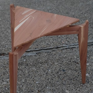 May include: A triangular wooden table with three legs. The table is made of cedar wood and has a natural wood finish.