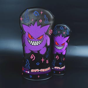 Puede incluir: Dos fundas negras para la cabeza del palo de golf con un diseño de Gengar morado, ojos rojos y una amplia sonrisa. Las fundas tienen detalles bordados, incluyendo espirales, estrellas y el texto "#094-GENGAR".