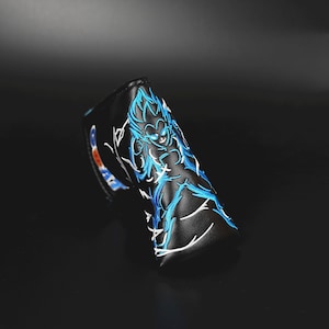 May include: Black golf club head cover featuring a blue and white embroidered anime character design. The cover is made of a leather-like material and has white stitching. The design depicts a character with spiky hair and energy effects.