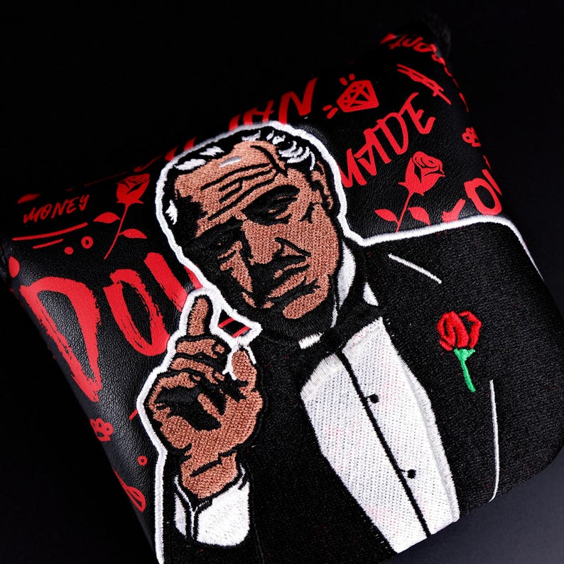 May include: Black golf club head cover featuring an embroidered image of a man in a tuxedo, with a red rose on the lapel. The cover has red text and rose graphics on a black background. The man is pointing with his index finger.