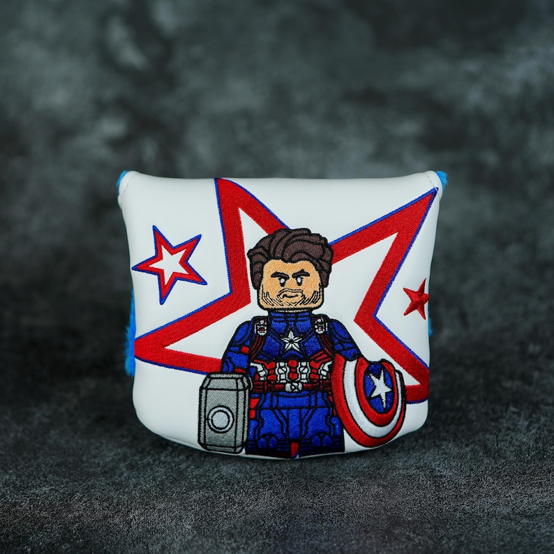 May include: White golf club head cover with a Captain America design. It features a red, white, and blue colour scheme, a star pattern, and an embroidered Captain America character. The cover is trimmed with blue piping.
