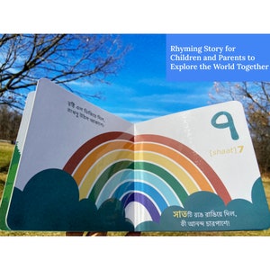 Puede incluir: Un libro infantil colorido con un arco&iacute;ris en la portada. El libro est&aacute; abierto en una p&aacute;gina con el n&uacute;mero 7 escrito en bengal&iacute; y la palabra "shaat" en ingl&eacute;s. El texto en la p&aacute;gina dice: "Llovi&oacute; y moj&oacute; todo, un arco&iacute;ris apareci&oacute; en el cielo. Siete colores lo pintaron, &iexcl;qu&eacute; alegr&iacute;a por todas partes!"