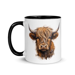 Peut inclure: Mug en céramique blanche avec un bord noir. La tasse présente une illustration aquarelle d'une vache Highland brune avec de longs poils hirsutes.