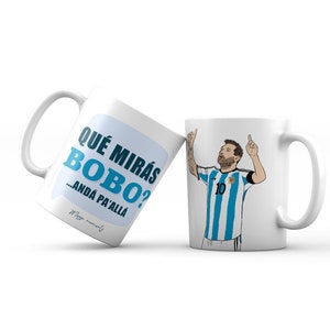Könnte beinhalten: Zwei weiße Keramikbecher. Ein Becher zeigt eine Comic-Illustration eines Fußballspielers in einem blau-weiß gestreiften Trikot mit der Nummer 10 auf der Vorderseite. Der andere Becher hat eine blaue Sprechblase mit dem Text "QUE MIRAS BOBO? ...ANDA PA'ALLA" auf Spanisch. Der Text "Mien moments" ist in einer kleineren Schrift unterhalb der Sprechblase gedruckt.