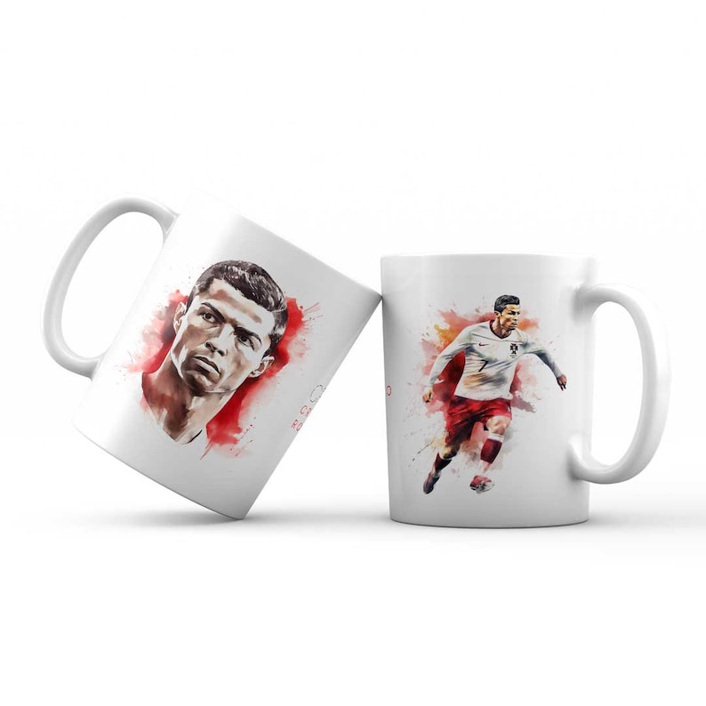 May include: Two white ceramic mugs with a watercolour design featuring Cristiano Ronaldo. One mug shows a close-up portrait of Ronaldo, while the other shows him playing football.