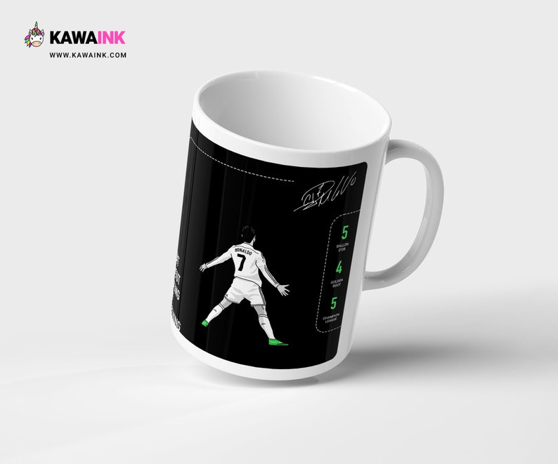 May include: White ceramic mug featuring a black and white illustration of a football player in action. The player is wearing a white jersey with the number 7 on it. The mug has a black background with white text that says "Ronaldo" and "Ball".