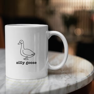 May include: White ceramic mug with a black line drawing of a goose and the text "silly goose" printed on the front.