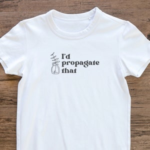 Peut inclure: T-shirt blanc avec un graphique noir d'une plante dans un bocal et le texte "J'aimerais propager &ccedil;a".