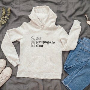 Peut inclure: Un sweat &agrave; capuche gris clair avec un motif noir qui dit "J'aimerais propager &ccedil;a" et une petite illustration d'une plante dans un bocal.