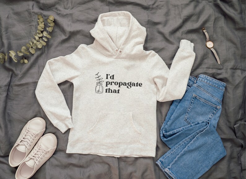 Peut inclure: Un sweat &agrave; capuche gris clair avec un motif noir qui dit "J'aimerais propager &ccedil;a" et une petite illustration d'une plante dans un bocal.