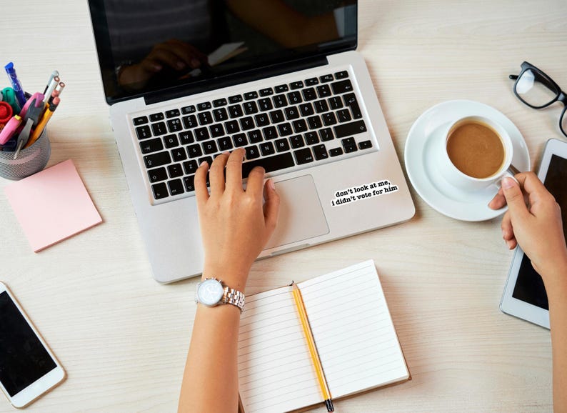 K&ouml;nnte beinhalten: Eine Person tippt auf einem Laptop mit einem Aufkleber auf dem Trackpad, auf dem steht: "Schau mich nicht an, ich habe nicht f&uuml;r ihn gestimmt."