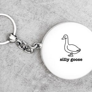 May include: White keychain with a black outline of a goose and the text "silly goose".
