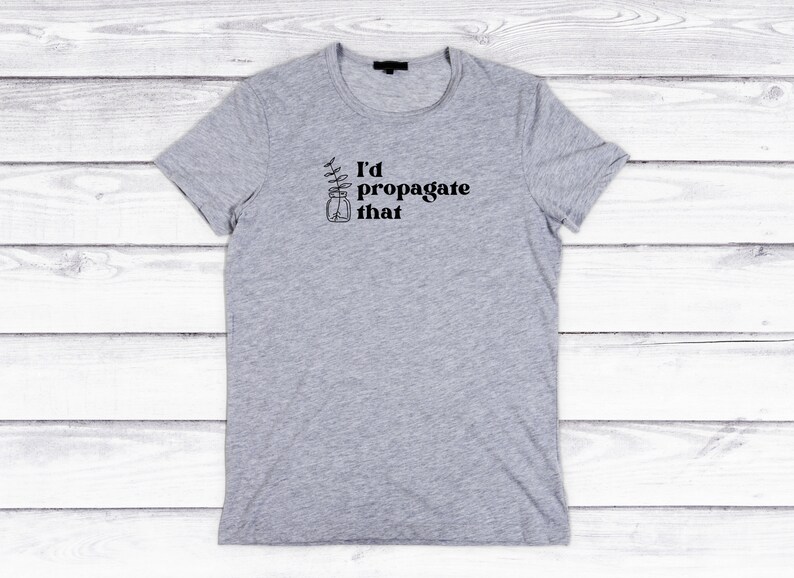 Peut inclure: Un t-shirt gris avec le texte "I'd propagate that" et un dessin d'une plante dans un bocal.