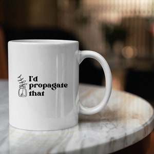 Peut inclure: Une tasse en c&eacute;ramique blanche avec un motif noir d'une plante dans un bocal et le texte "J'aimerais propager &ccedil;a".