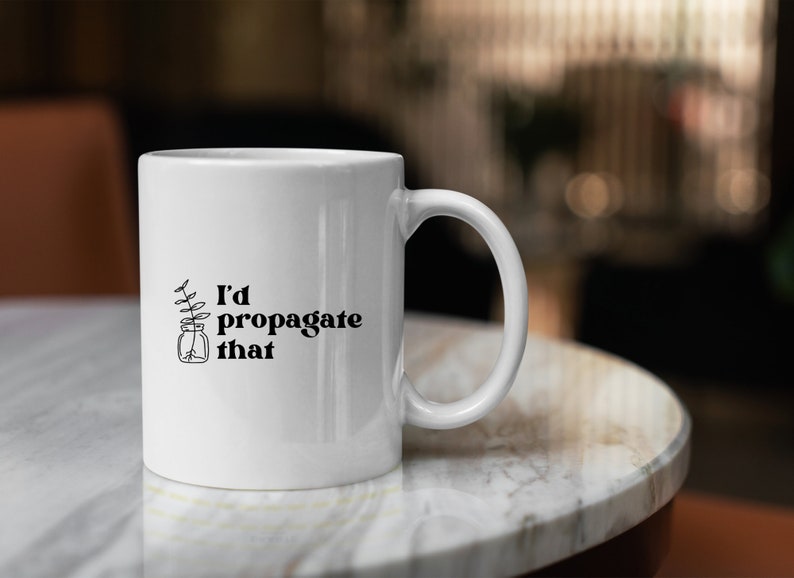Peut inclure: Une tasse en c&eacute;ramique blanche avec un motif noir d'une plante dans un bocal et le texte "J'aimerais propager &ccedil;a".
