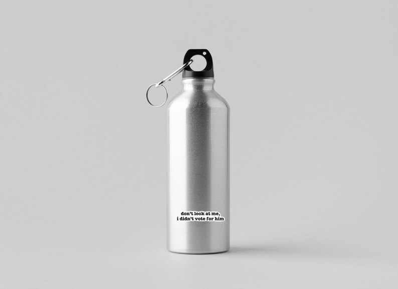 K&ouml;nnte beinhalten: Eine silberne Wasserflasche mit schwarzem Deckel und einer Trageschlaufe. Die Flasche hat einen Aufkleber mit dem Text "Schau mich nicht an, ich habe nicht f&uuml;r ihn gestimmt".