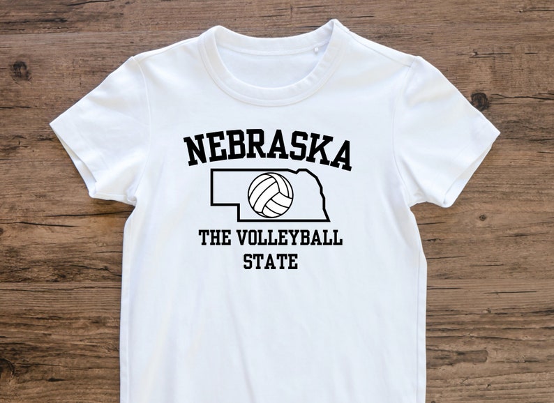 May include: White t-shirt with black text that reads "Nebraska The Volleyball State" and an outline of the state of Nebraska with a volleyball inside.