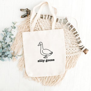 May include: A white canvas tote bag with a black line drawing of a goose and the text "silly goose".