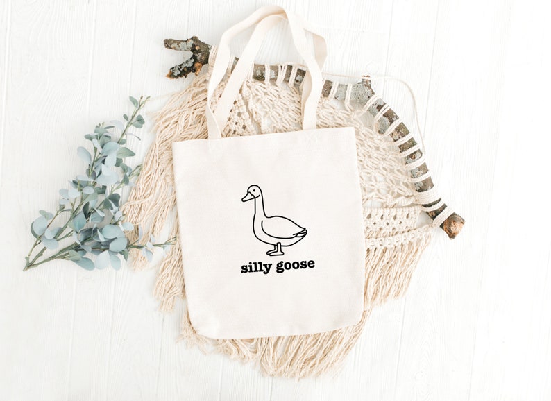 May include: A white canvas tote bag with a black line drawing of a goose and the text "silly goose".