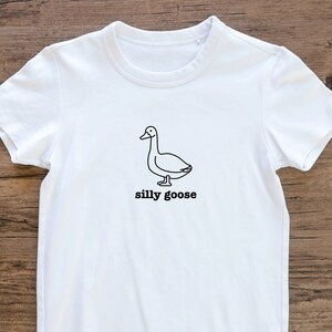May include: White t-shirt with a black line drawing of a goose and the text "silly goose" printed on the front.