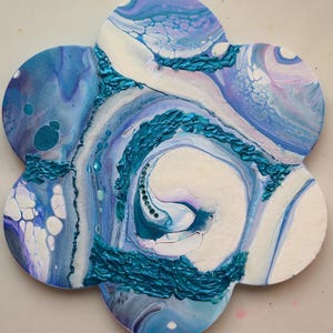 Könnte beinhalten: Ein blumenförmiges Wandkunstobjekt mit einem Acryl-Gießdesign in Blau-, Lila- und Weißtönen. Die Oberfläche zeigt marmorierte Farbmuster mit erhabenen, strukturierten türkisfarbenen Farbakzenten, die in geschwungenen Linien über die Blütenblätter verlaufen.