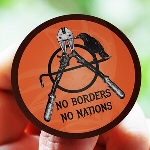 Può includere: Un adesivo rotondo arancione con un'illustrazione in bianco e nero di un corvo appollaiato su un paio di tronchesi incrociati. L'adesivo ha il testo "NO BORDERS NO NATIONS" in nero.