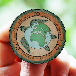 Puede incluir: Una pegatina redonda verde y marrón con el texto "Save the planet" repetido dos veces. La pegatina presenta una tortuga marina verde con un globo terráqueo azul y verde en su espalda.