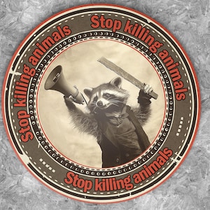 Peut inclure: Un autocollant circulaire brun et rouge avec le texte "Stop killing animals" répété trois fois autour du bord. Au centre, un raton laveur portant un costume tient un mégaphone et un couteau.