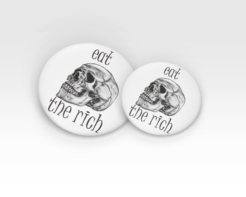 May include: Two white round buttons with black text and a black and white skull graphic. The larger button says "eat the rich" and the smaller button says "eat the rich".