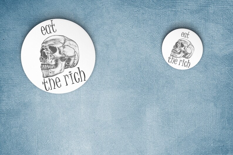 May include: Two white round buttons with a black and white skull graphic and the text "eat the rich". The larger button is on the left and the smaller button is on the right.