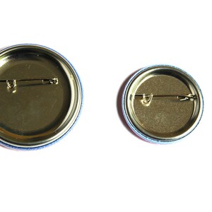 May include: Two round button pins with a gold metal back and a safety pin closure. The larger pin has a blue and pink border, and the smaller pin has a blue and red border.