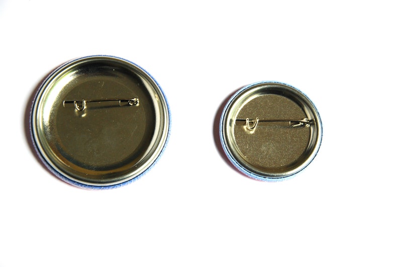 May include: Two round button pins with a gold metal back and a safety pin closure. The larger pin has a blue and pink border, and the smaller pin has a blue and red border.