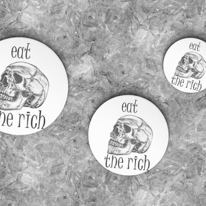 May include: Three white round buttons with a black skull and the text "eat the rich" on each.