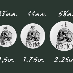 May include: Three white round buttons with a black and white skull graphic and the text "eat the rich". The buttons are 1.5 inches, 1.75 inches, and 2.25 inches in diameter.