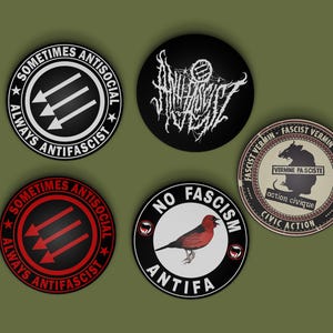 Puede incluir: Cinco botones redondos con lemas antifascistas. Los botones son negros, blancos y rojos con texto blanco. Los lemas incluyen "Sometimes Antisocial Always Antifascist", "No Fascism Antifa" y "Fascist Vermin - Vermine Fasciste - Action Civique - Civic Action".