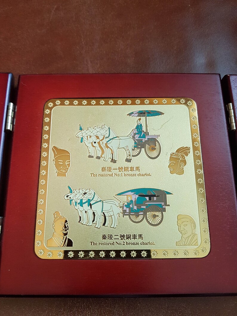 May include: A wooden plaque with a gold-colored frame and two images of bronze chariots. The text on the plaque reads "秦陵一號銅車馬 The restored No:1 bronze chariot." and "秦陵二號銅車馬 The restored No:2 bronze chariot."