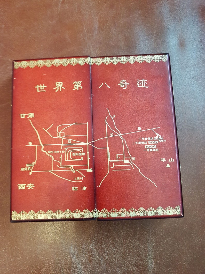 May include: A red leather-bound box with gold accents and a map of the Terracotta Army in Xi'an, China. The box has the text "World Eighth Wonder" in Chinese characters on the front.