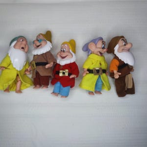 Può includere: Una collezione di cinque statuette di Biancaneve e i Sette Nani. Ogni nano è vestito con un abito di colore diverso, tra cui giallo, marrone, rosso e blu. Hanno barbe bianche e sono in varie pose.