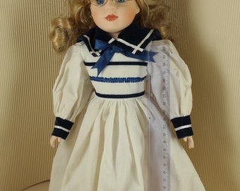 Muñeca coleccionable de porcelana vintage: Marinera con vestido blanco y azul, ojos cerrados.