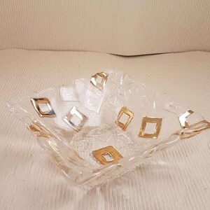 May include: A clear glass bowl with a square shape and gold geometric designs. The bowl is perfect for serving snacks or fruit.