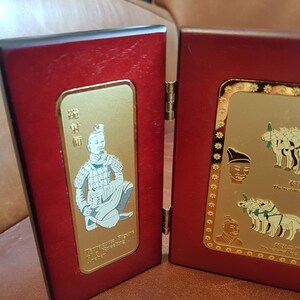 May include: A wooden display case with two hinged panels. The left panel features a gold-colored plaque with a white image of a warrior figure. The right panel features a gold-colored plaque with three white images of horses and a white image of a warrior's head. The text on the plaques reads "Terracotta Figure Of The Emperor's Army" and "The Emperor's Army".