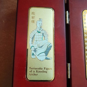 May include: A wooden display case with a gold plaque featuring a terracotta figure of a kneeling archer. The plaque has the text "Terracotta Figure of a Kneeling Archer" and Chinese characters in gold.