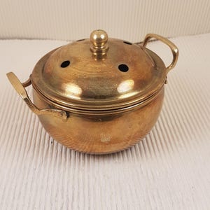 May include: A small, round, brass incense burner with a lid and two handles. The lid has several small holes for the incense to burn through.