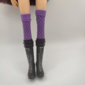 Pode incluir: Pernas de boneca usando meias roxas de rede e botas de combate pretas. As botas t&ecirc;m cadar&ccedil;os e fivelas. A boneca tamb&eacute;m est&aacute; usando shorts pretos.