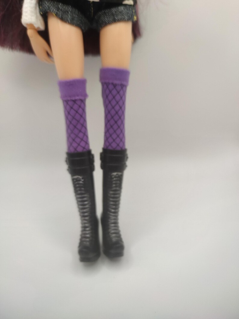 Pode incluir: Pernas de boneca usando meias roxas de rede e botas de combate pretas. As botas t&ecirc;m cadar&ccedil;os e fivelas. A boneca tamb&eacute;m est&aacute; usando shorts pretos.