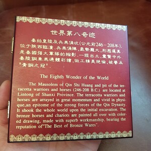 May include: A red wooden box with gold trim and a gold inscription that reads "The Eighth Wonder of the World." The inscription is in both English and Chinese. The box is about the size of a small book and has a hinged lid.