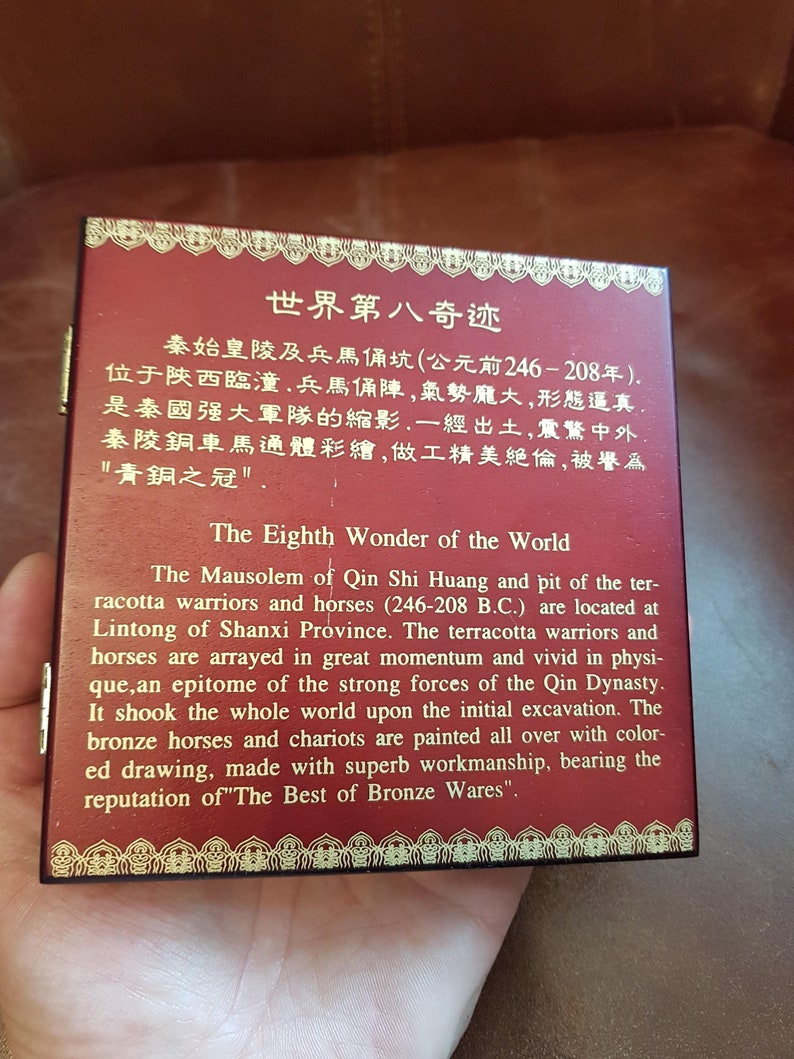 May include: A red wooden box with gold trim and a gold inscription that reads "The Eighth Wonder of the World." The inscription is in both English and Chinese. The box is about the size of a small book and has a hinged lid.