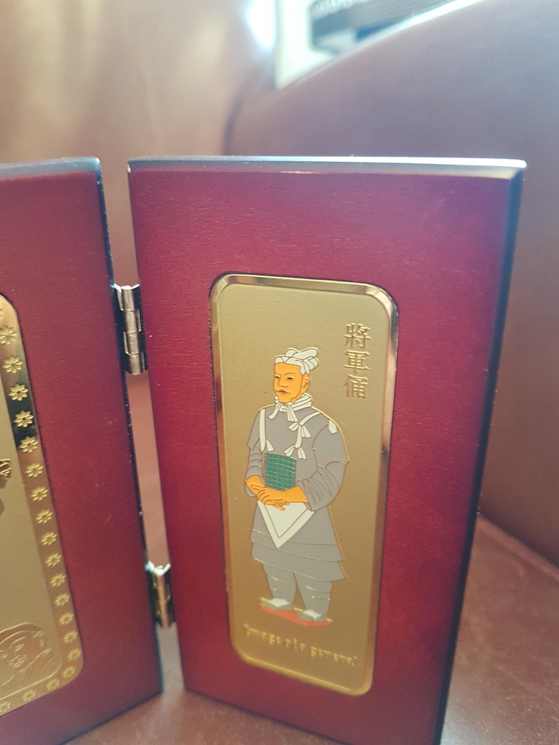 May include: A red wooden frame with a gold-colored inset featuring a portrait of a person in traditional clothing. The person is wearing a white hat and a gray robe. The text "將軍" is written in gold on the right side of the frame.